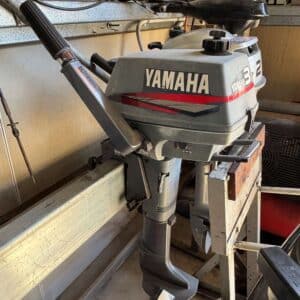 The side of a Yamaha 3 horsepower 2 stroke outboard with tiller steering sitting on a motor rack