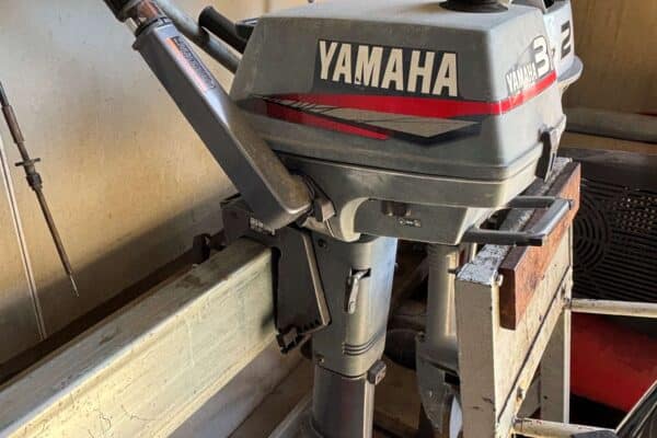 The side of a Yamaha 3 horsepower 2 stroke outboard with tiller steering sitting on a motor rack