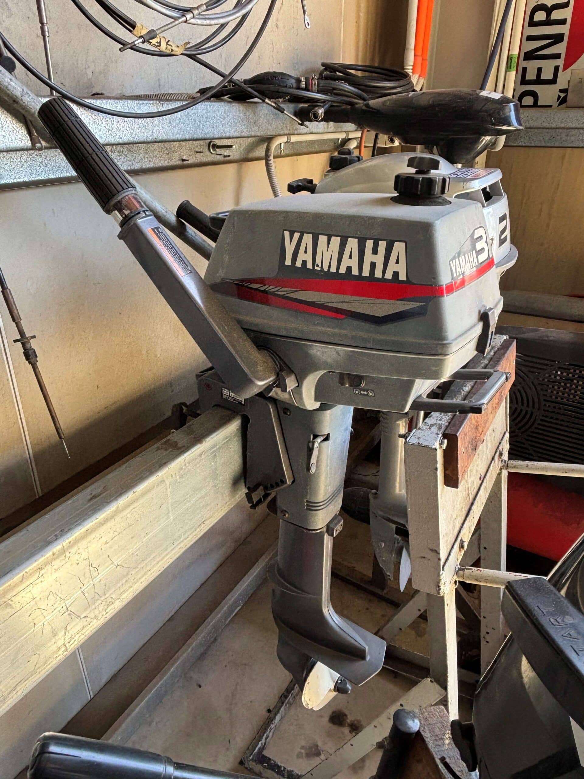 The side of a Yamaha 3 horsepower 2 stroke outboard with tiller steering sitting on a motor rack